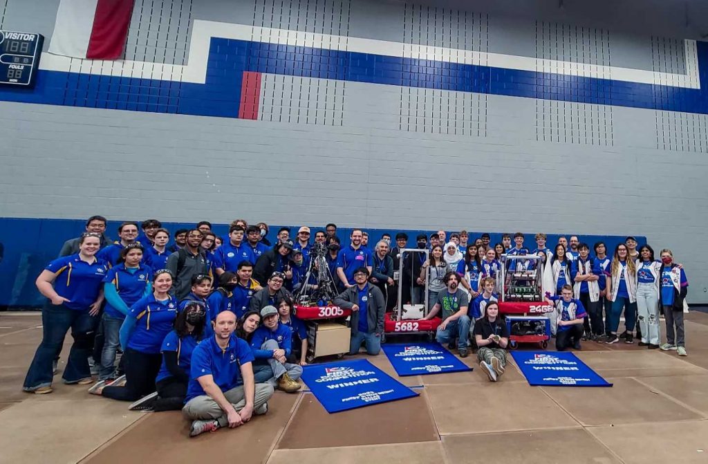 Image shows the captains and two members of the Dallas District winning alliance posed with their robots and blue champions banners